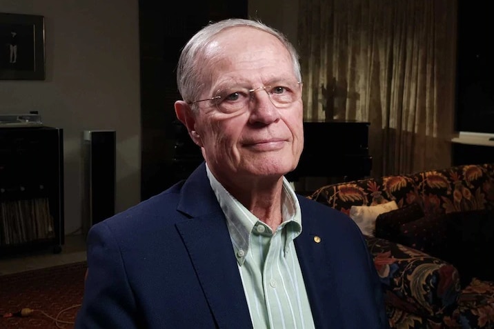 A man with glasses looks at the camera.