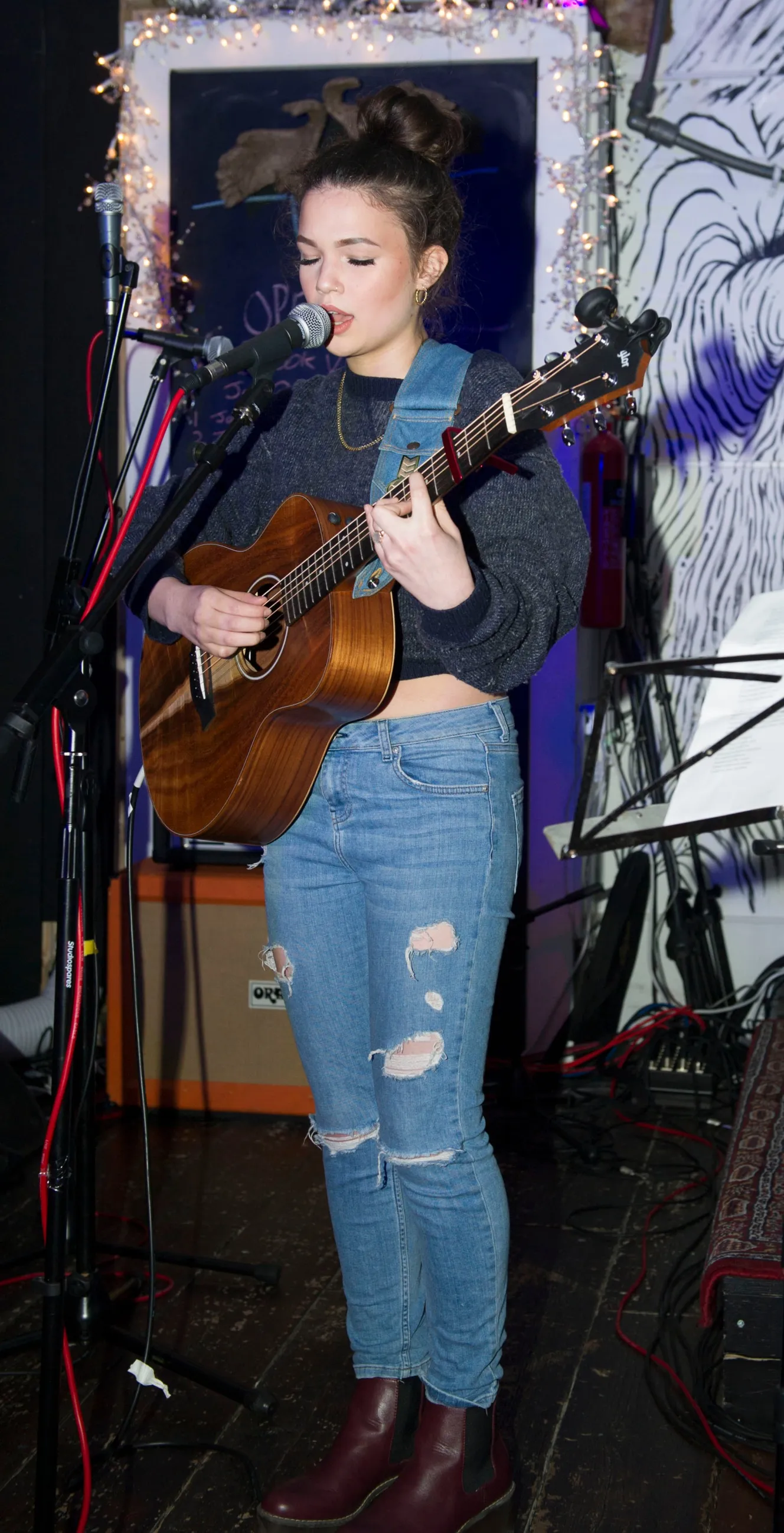 Lola Young singing into a microphone and playing an acoustic guitar.