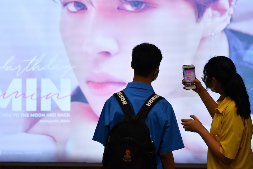 One person taking a picture of a K-pop idol while the other watch.