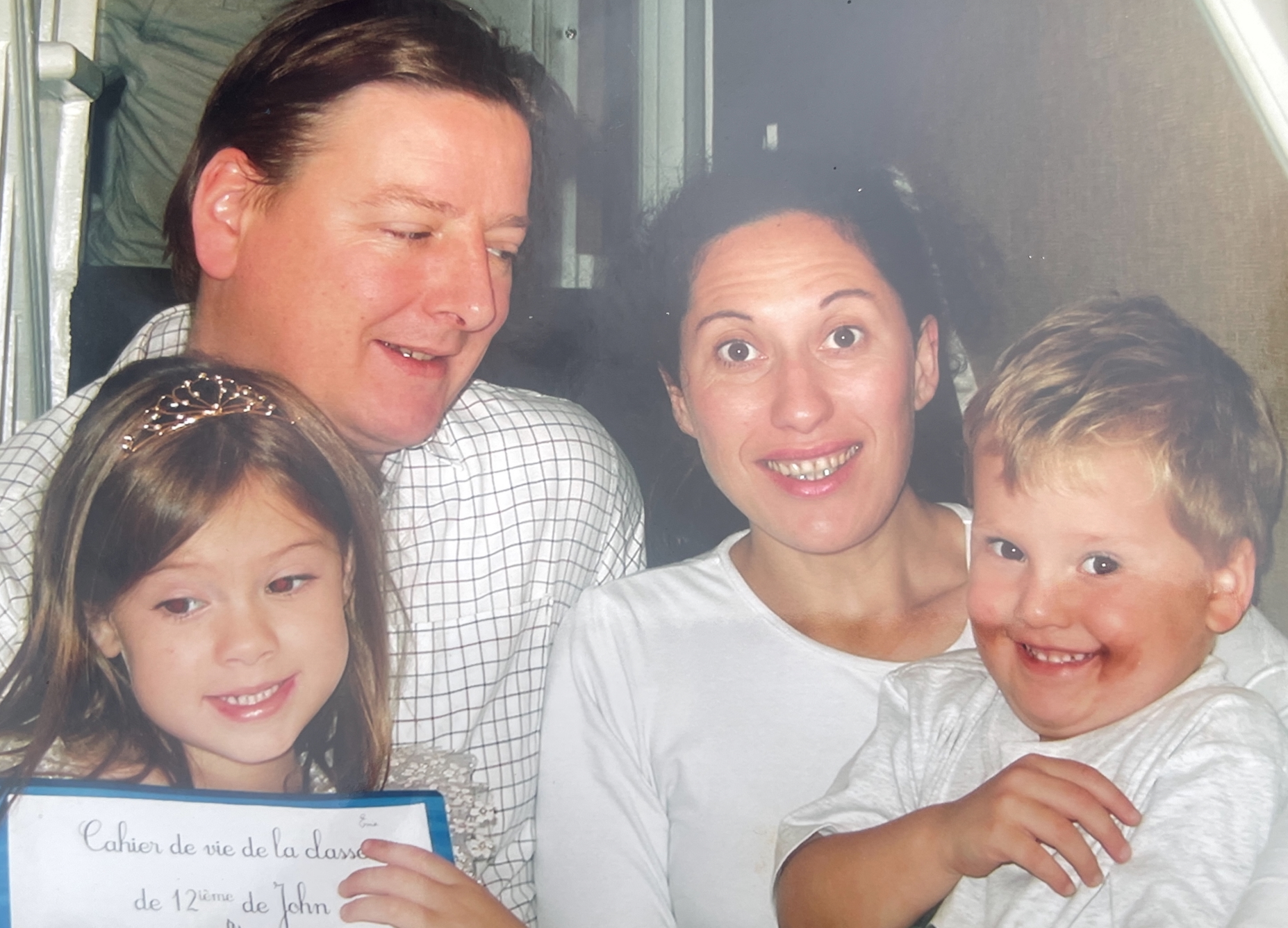 A family portrait of a father, mother, daughter with a tiara, and a young son with chocolate on his face.
