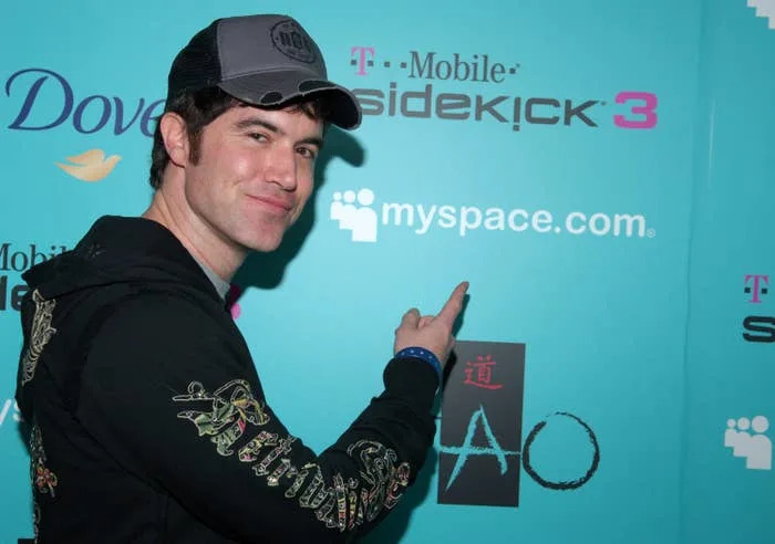Tom Anderson pointing at "myspace.com" logo on a sponsor wall