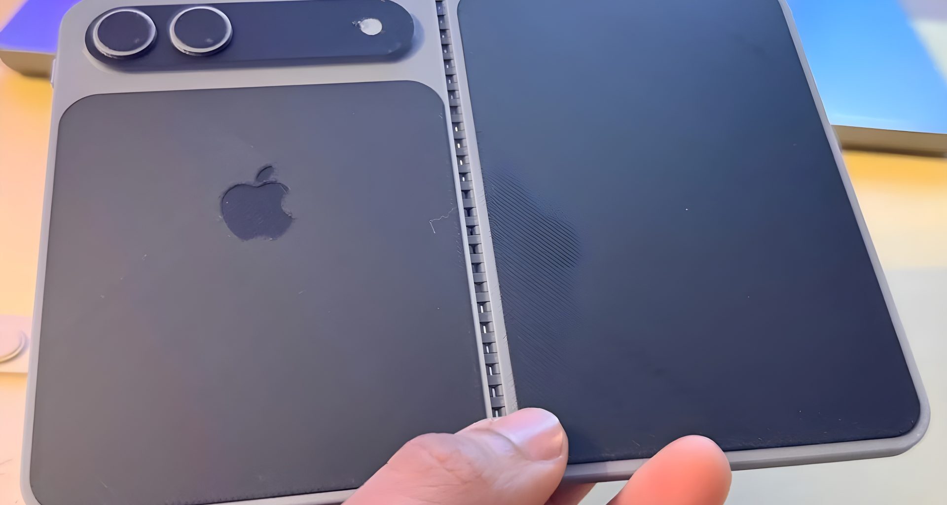 A person is holding a concept model of a foldable Apple device with a dual-camera setup and the Apple logo on the back.