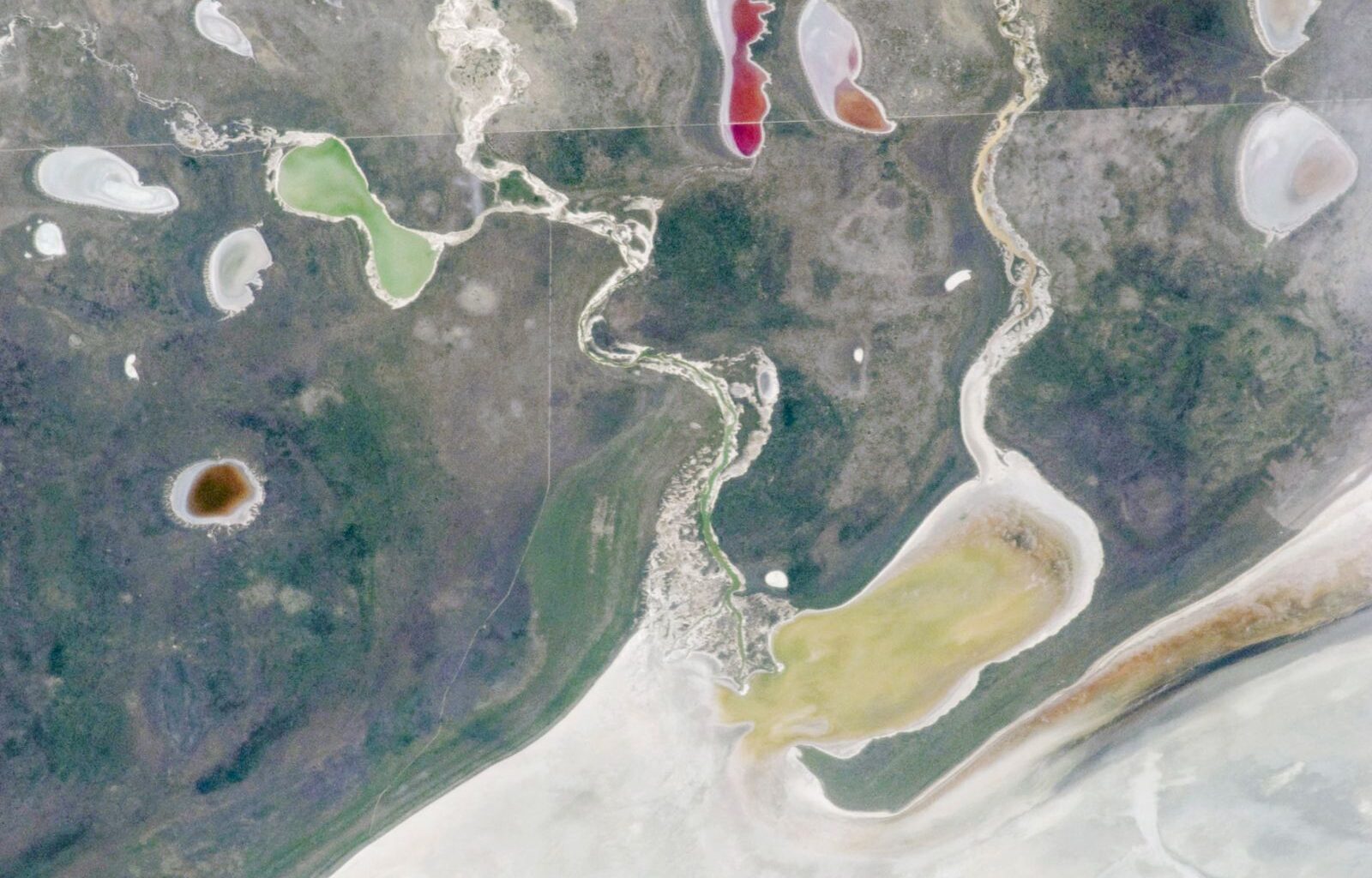 A satellite photo showing a pair of rivers and a series of colorful lakes surrounding a giant white expanse