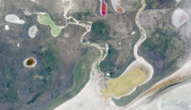 A satellite photo showing a pair of rivers and a series of colorful lakes surrounding a giant white expanse