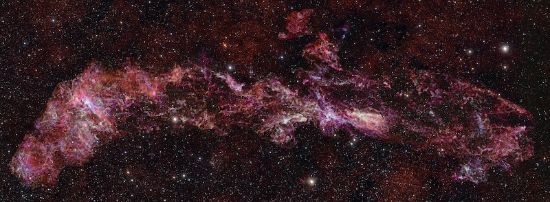 A band of reddish clouds with patches of white, against a black backdrop with stars.