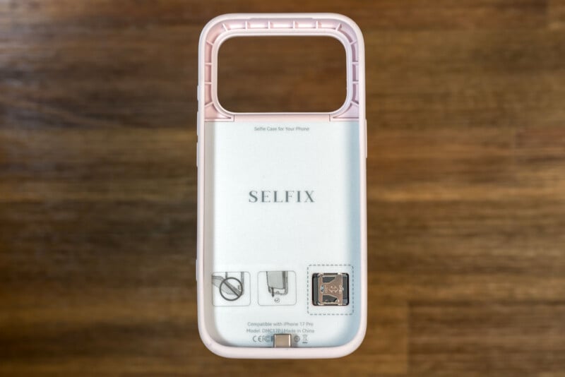 A pink and clear phone case labeled "SELFIX" lying on a wooden surface, designed for iPhone 7/8, with a large rectangular opening at the top and printed instructions visible on the back.