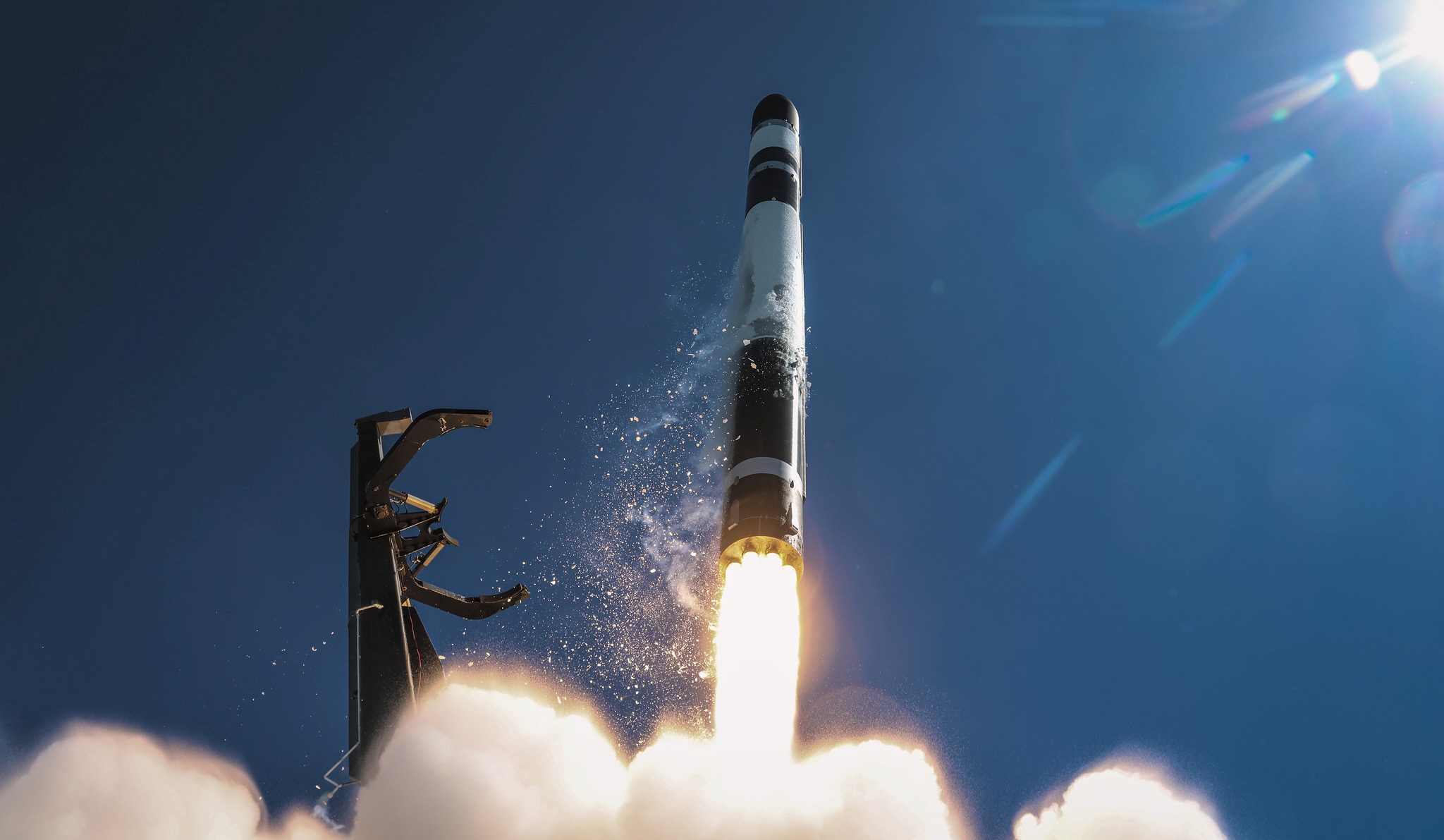 a black and white rocket launches into a blue sky