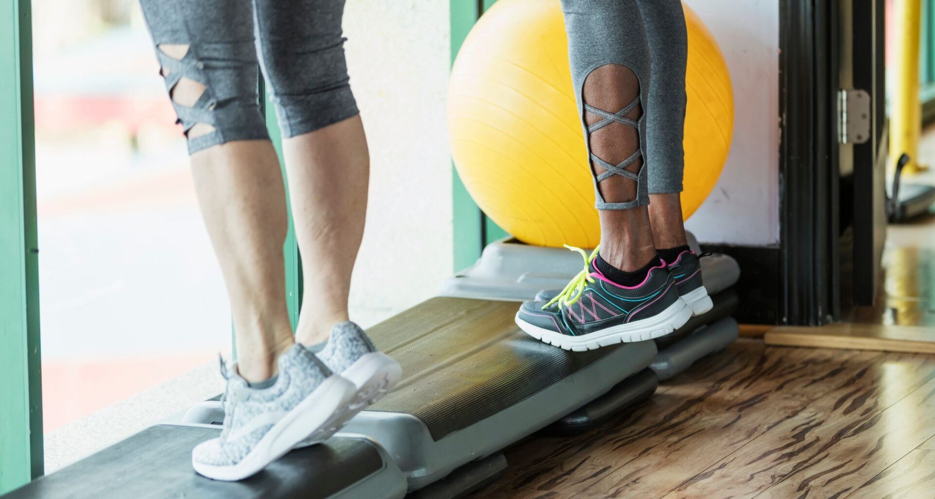 two pairs of legs stand on a workout step doing calf raises