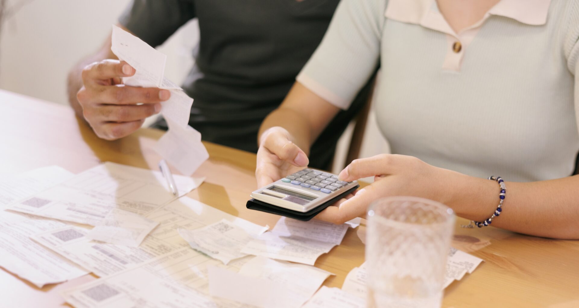 A man and woman seated at a table with papers, bills, receipts, and a calculator in front of them