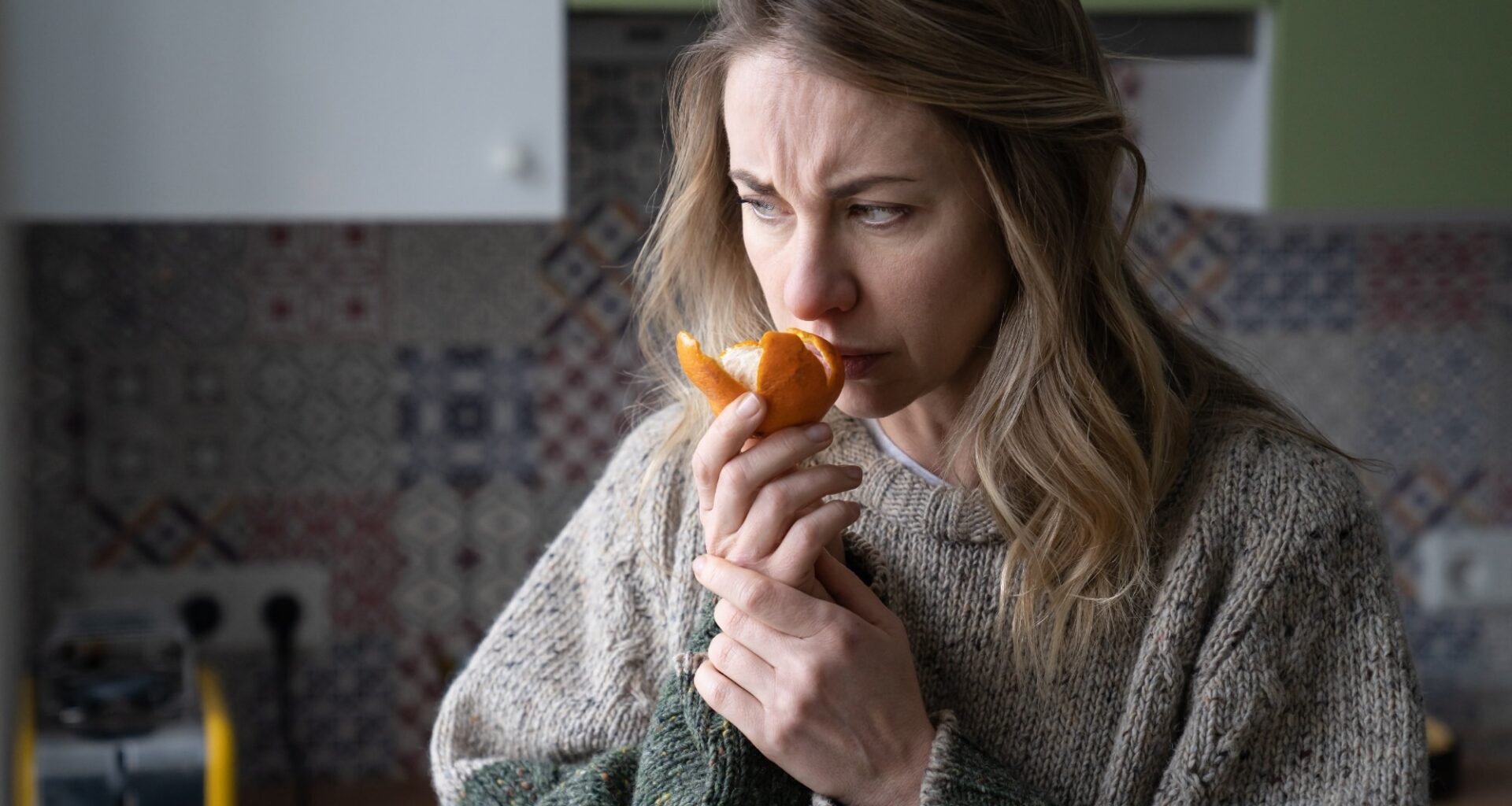 Sick woman trying to sense smell of fresh tangerine orange, has symptoms of Covid-19, corona virus infection - loss of smell and taste, standing at home.