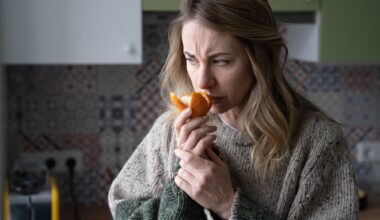 Sick woman trying to sense smell of fresh tangerine orange, has symptoms of Covid-19, corona virus infection - loss of smell and taste, standing at home.