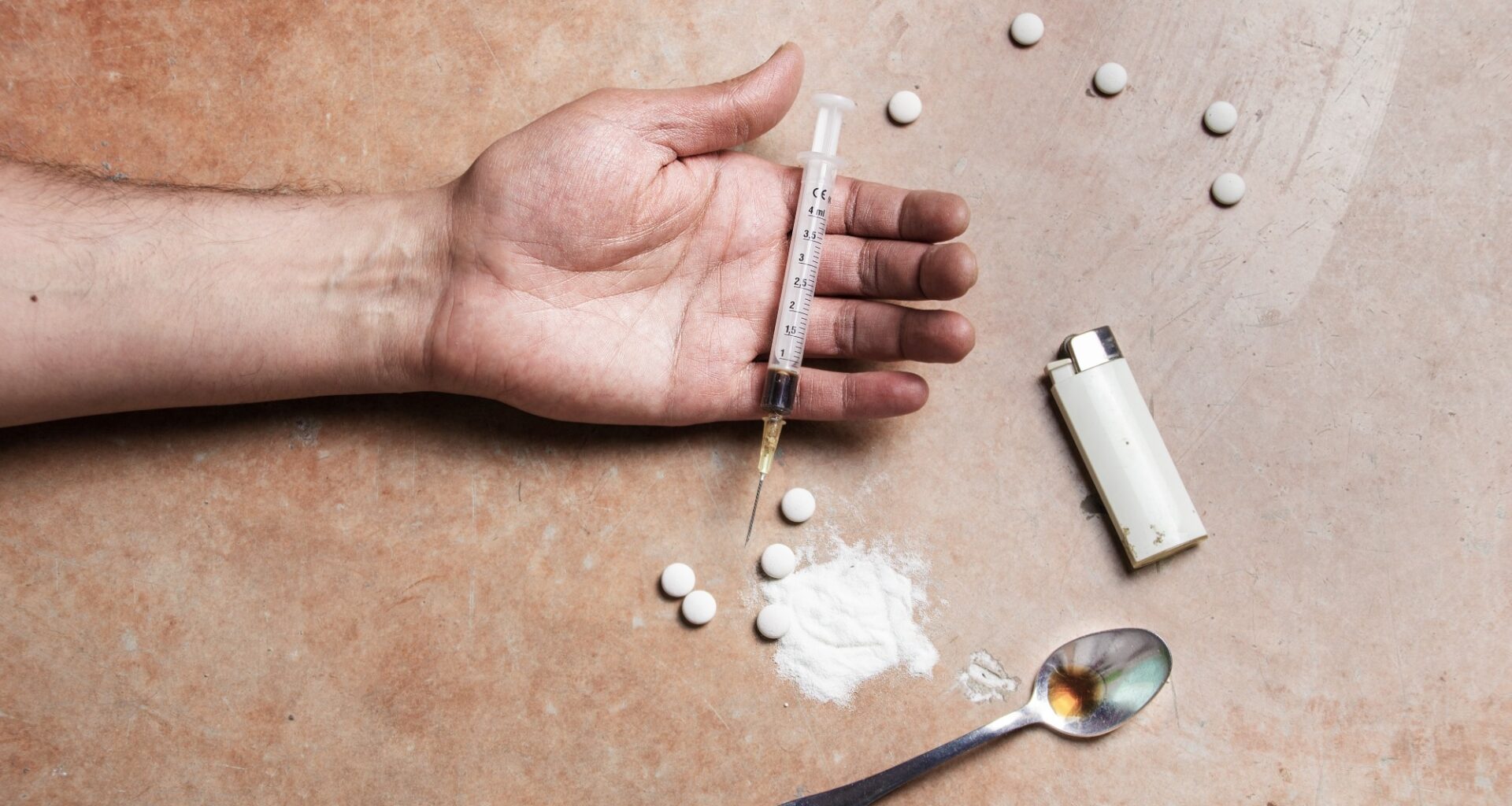 Close up shot of a drug addicts limp arm with drug paraphernalia lying next to it