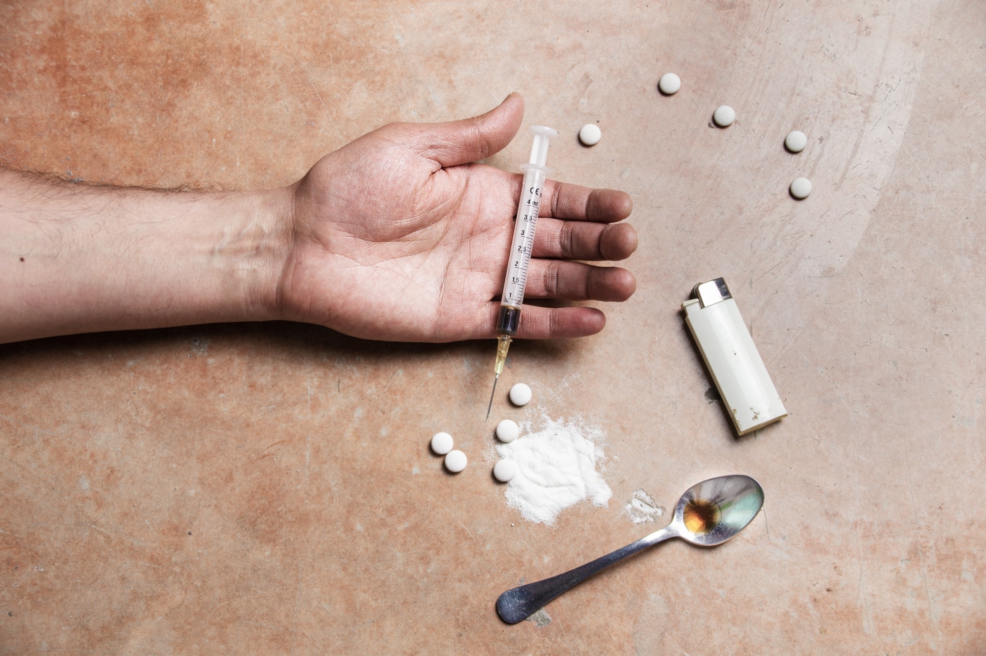 Close up shot of a drug addicts limp arm with drug paraphernalia lying next to it