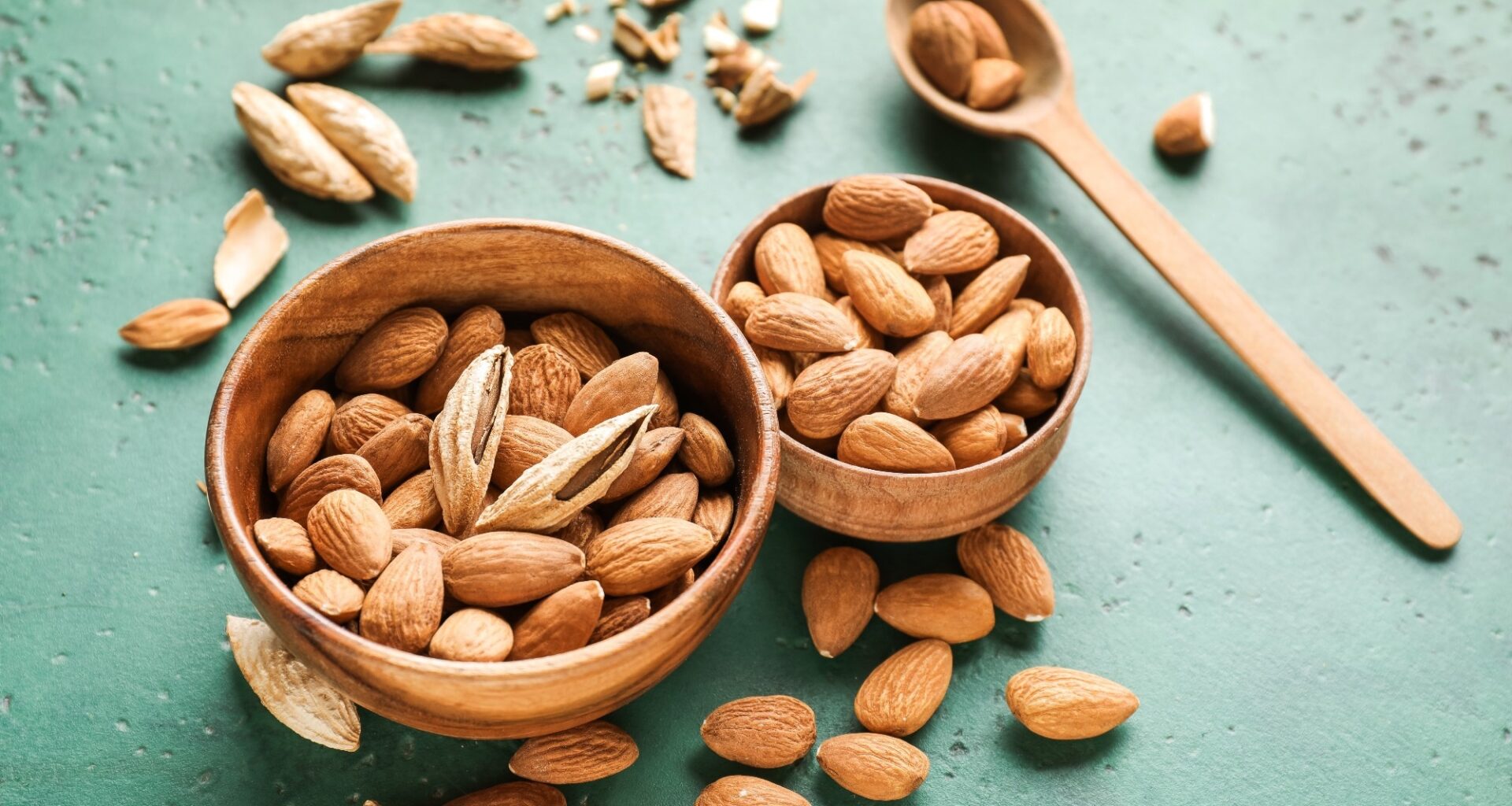 Bowls with tasty almonds on color background