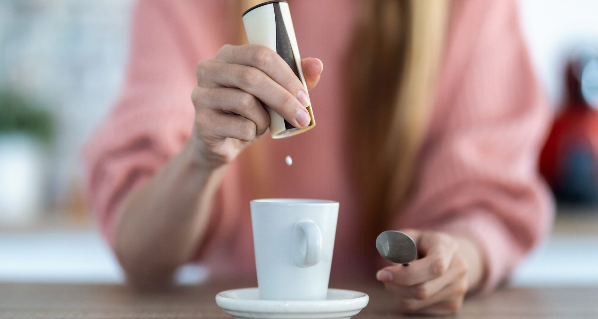 Close-up of woman hand throwing saccharin pills on coffee cup in the kitchen at home.