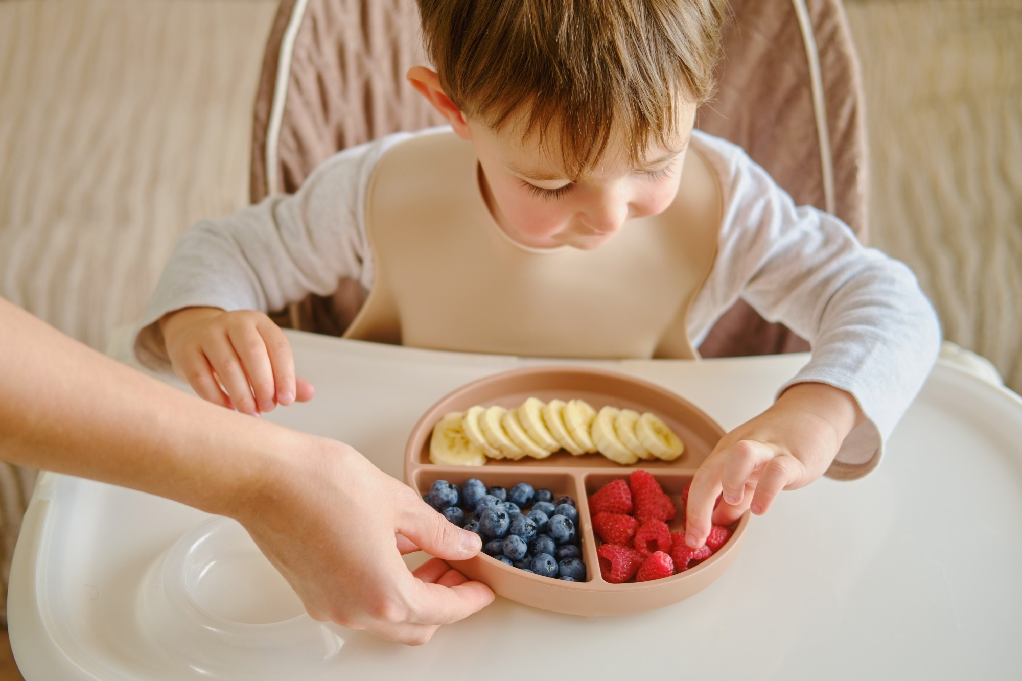 A mother woman gives her child a plate of fruits and berries