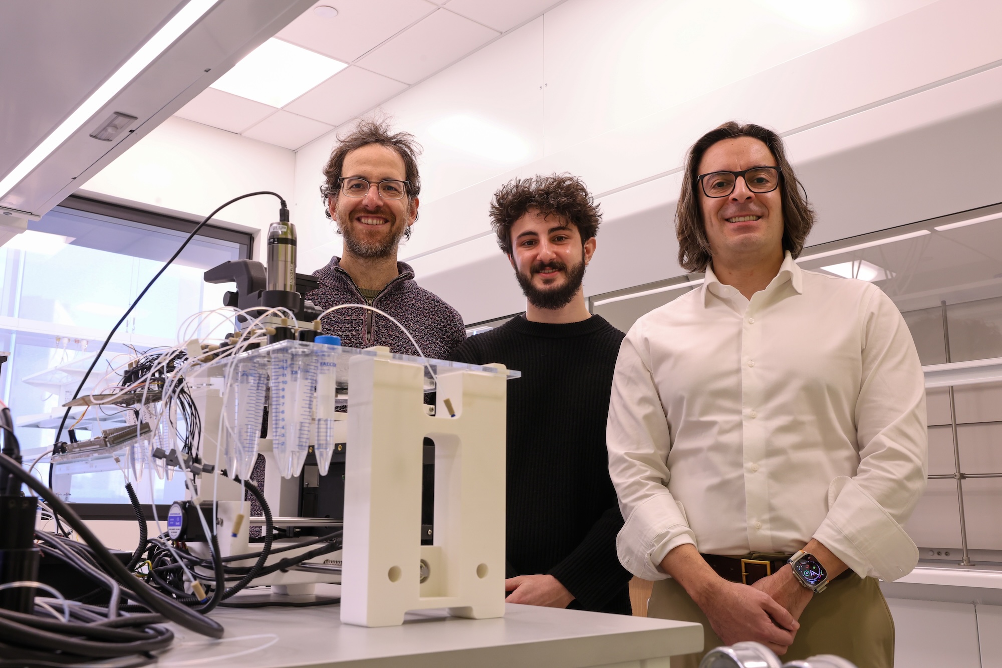 Three men stand shoulder to shoulder in the middle ground, with a robot on a lab bench in the foreground.