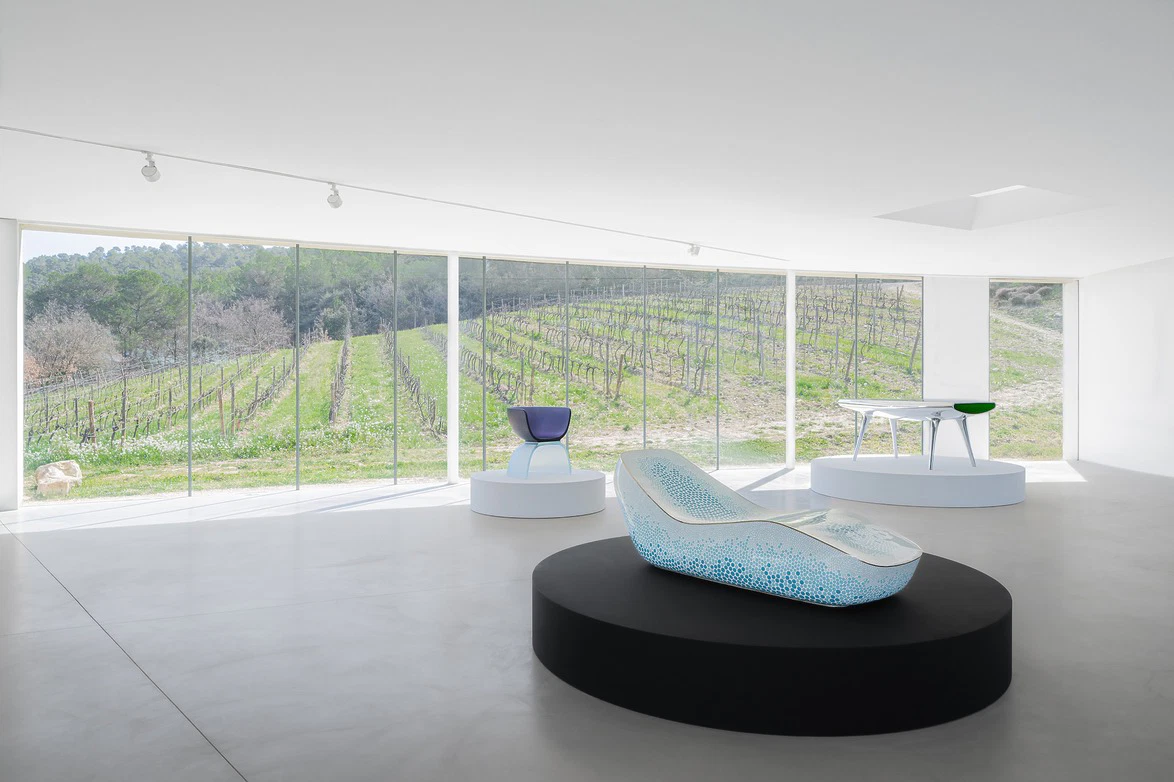 Modern minimalist showroom with designer furniture and panoramic vineyard view through large windows.