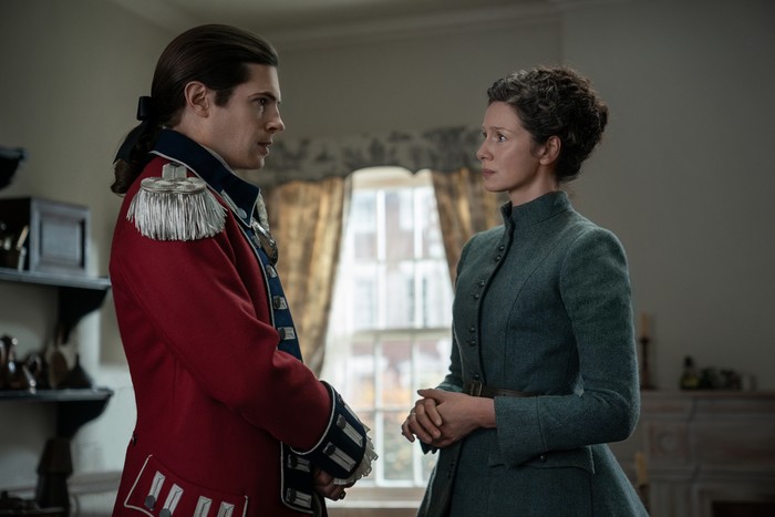 David Berry as Lord John Grey and Caitriona Balfe as Claire Fraser in Outlander season 7 part 2 standing in the middle of a room and staring at each other, mid-conversation.