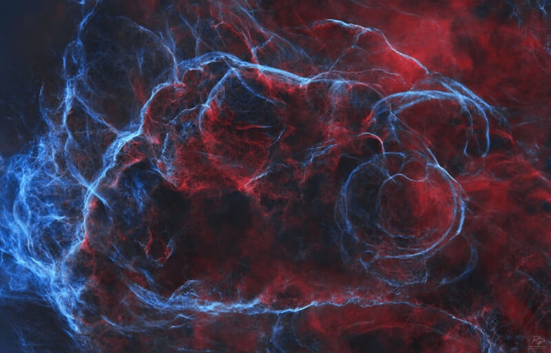 Swirling clouds of red and blue light intertwine against a dark background, creating an ethereal, nebula-like abstract pattern with delicate, wispy textures.