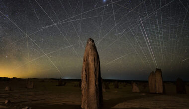 light trails of satellites in night sky with rock formation in foreground