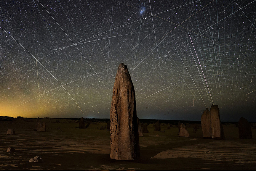 light trails of satellites in night sky with rock formation in foreground