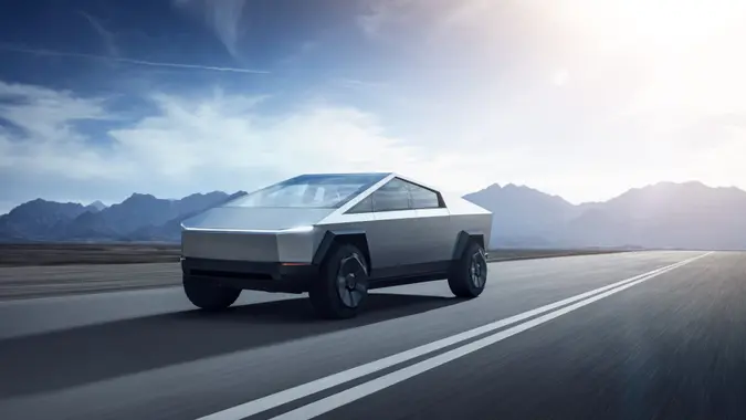 A Tesla Cybertruck on an empty road with mountains in the distance.