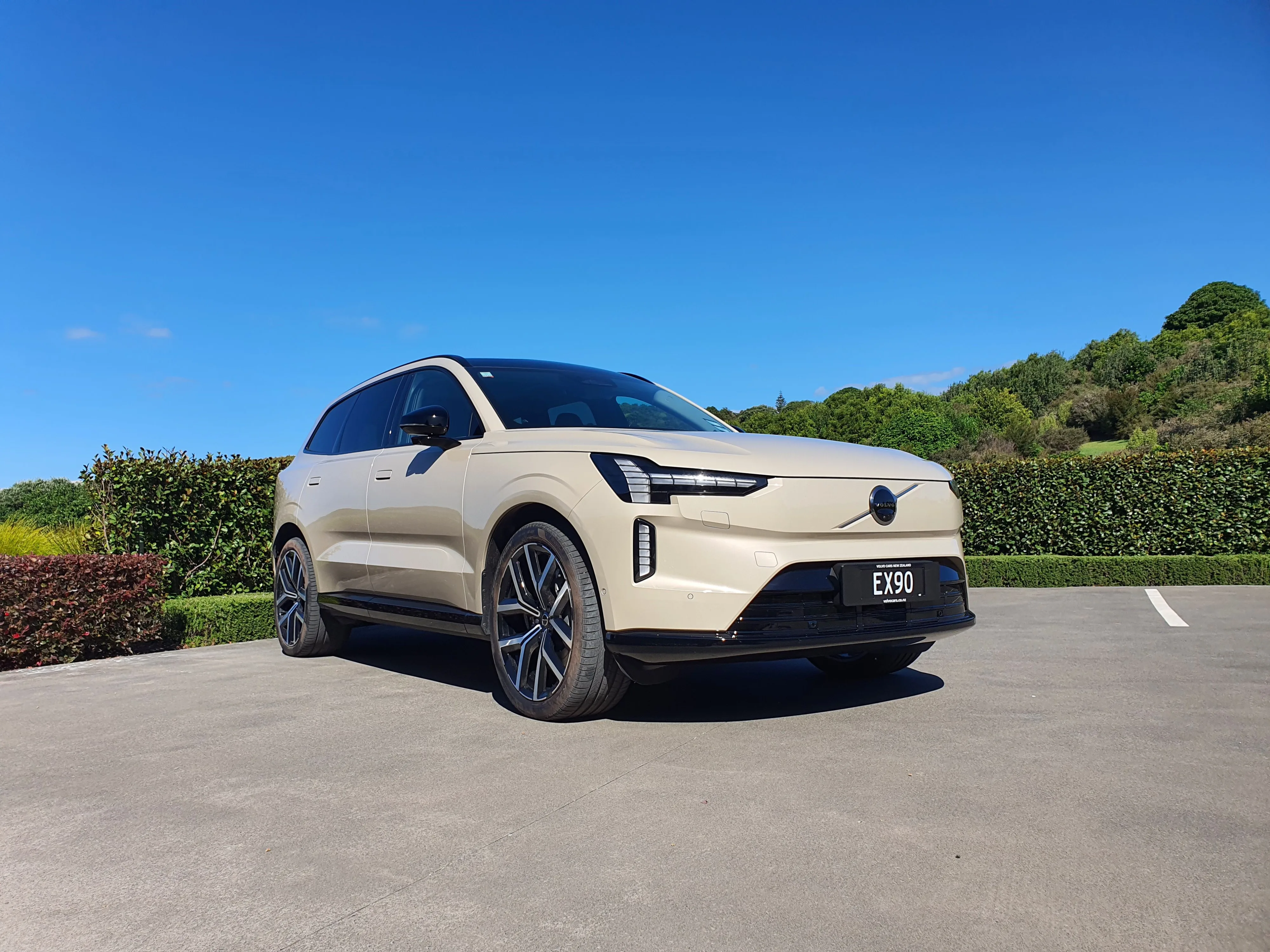 Front three quarters view of a Volvo EX90 in 'Sand Dune' outside The Tasting Room in The Landing Winery, Purerua Peninsula, Bay of Islands, New Zealand.