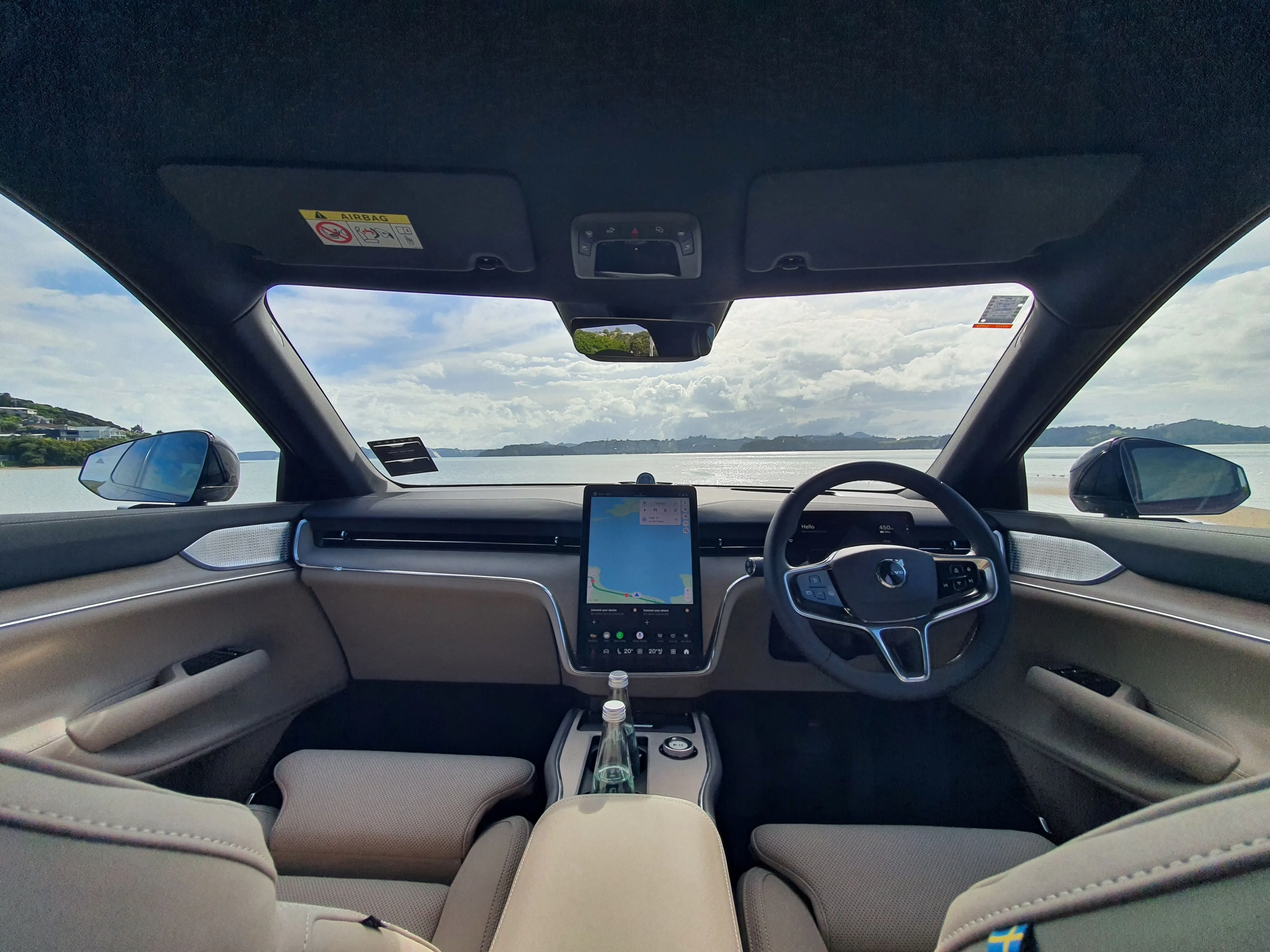 Interior view of a 2026 Volvo EX90 with an outlook of the ocean beside Paihia in the Bay of Islands, New Zealand.