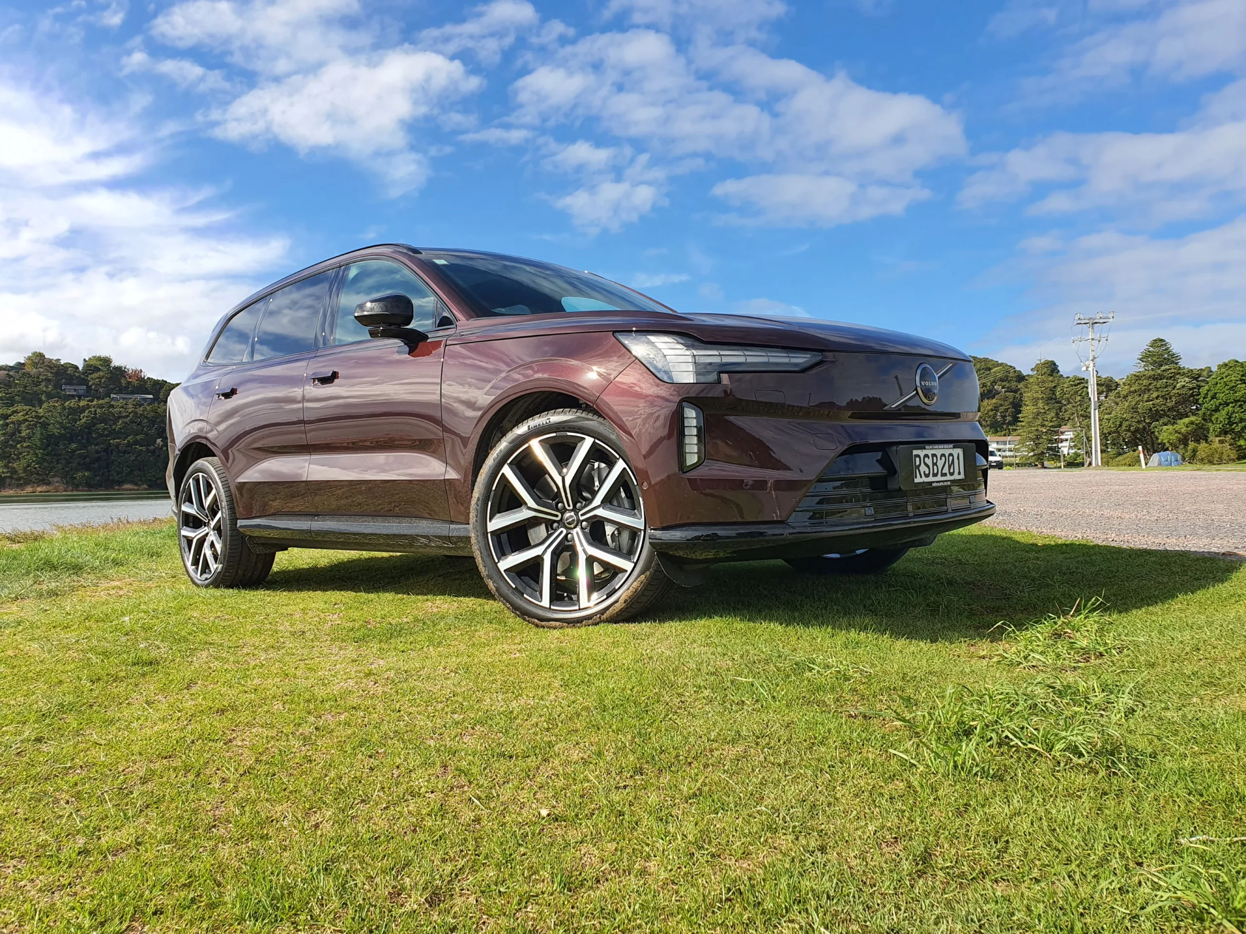 Front three quarters view of a Volvo EX90 in 'Mulberry Red', taken off a beach outside of Paihia, Bay of Islands, New Zealand.