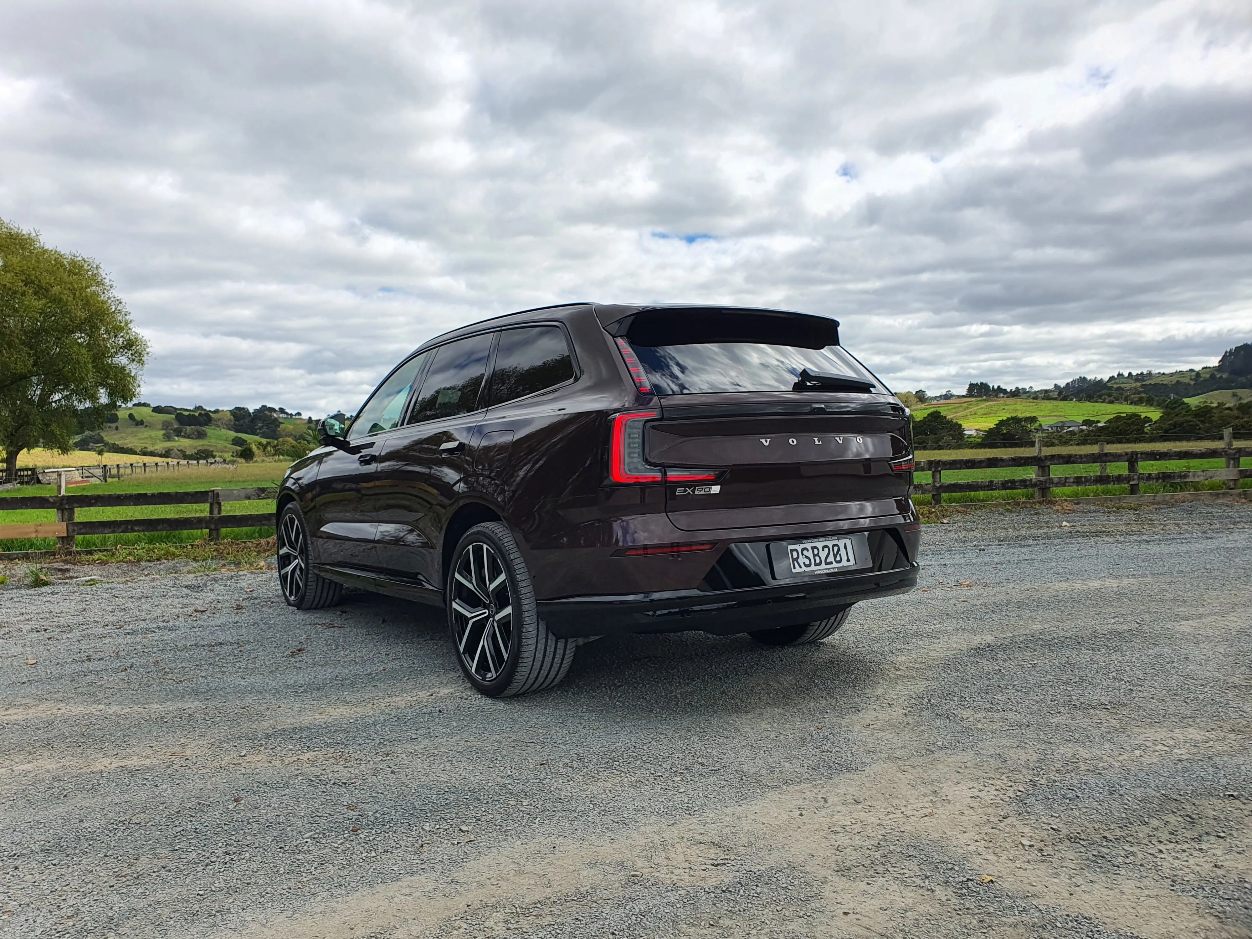 Rear three quarters view of a Volvo EX90 in 'Mulberry Red', taken in Northland, New Zealand.