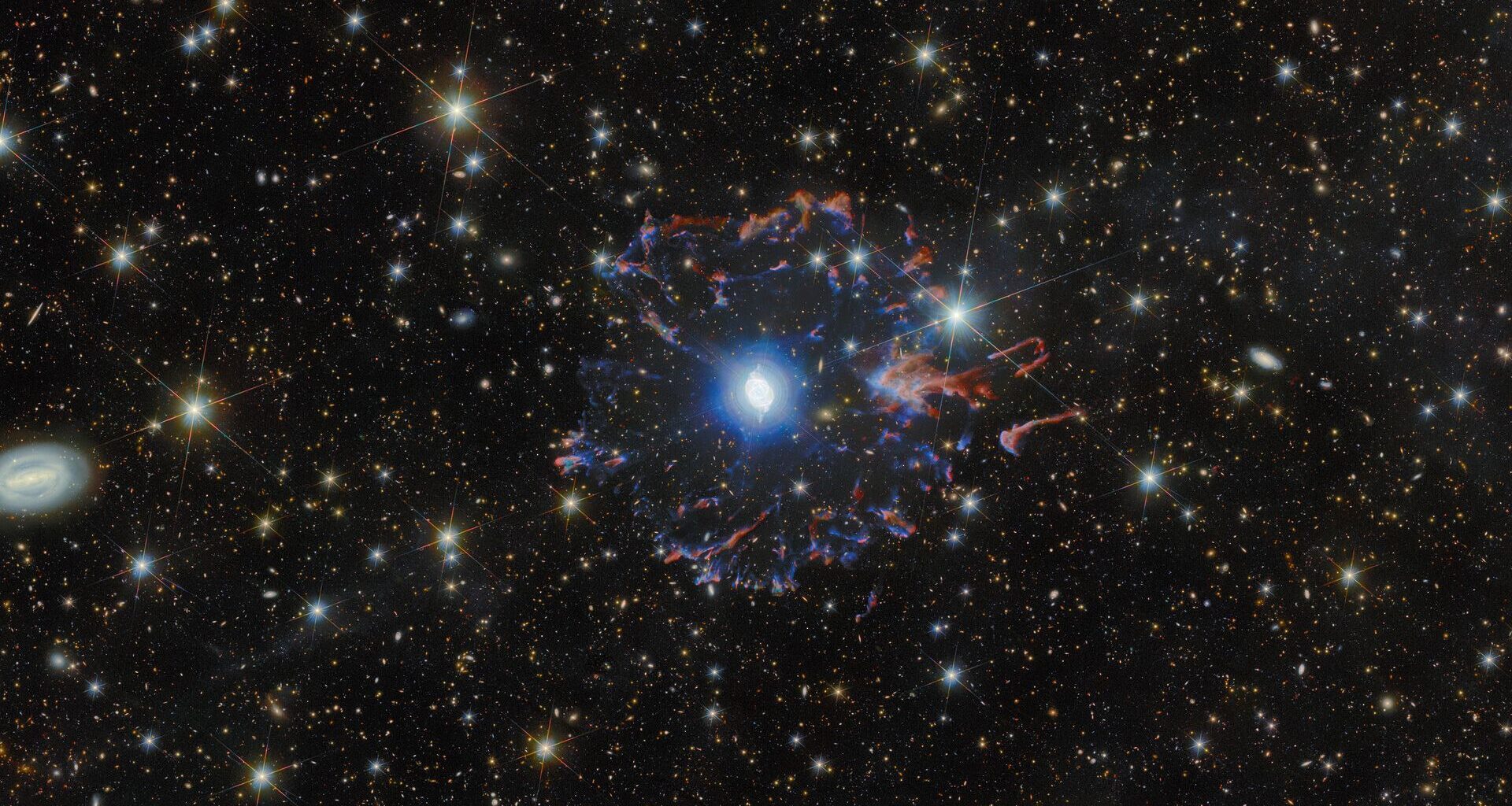 A view of the Cat's Eye Nebula, a blue ball of light surrounded by purple and red gas in a starry night sky