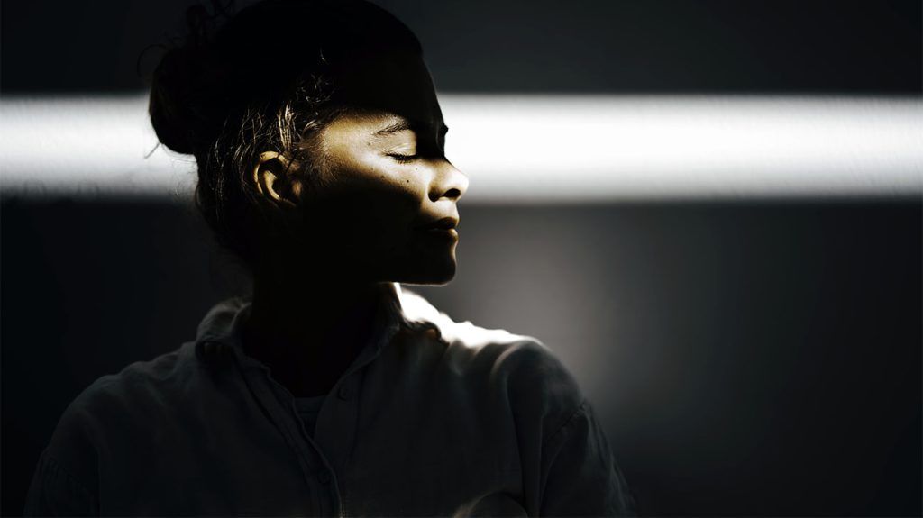 A woman's side profile as a ray of sunlight illuminates her closed eyes