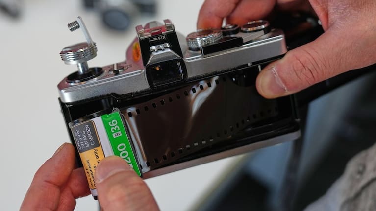 A journalist puts a film into an analogue camera.