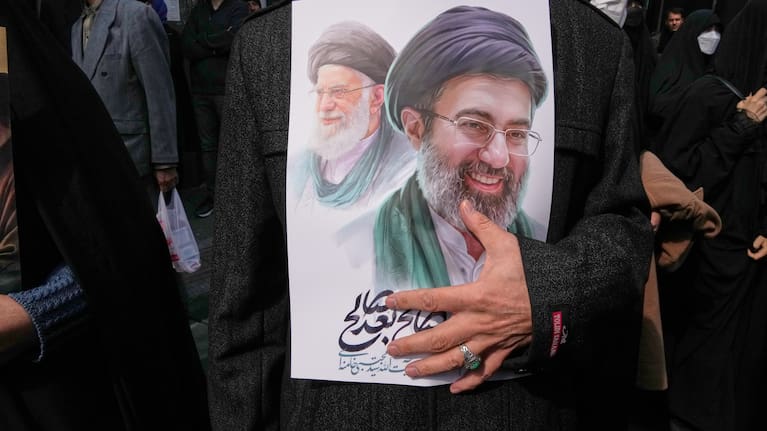 A mourner holds a poster depicting Ayatollah Mojtaba Khamenei, right, the successor to his late father Ayatollah Ali Khamenei, left, as supreme leader, during the funeral procession for senior Iranian military officials and civilians.