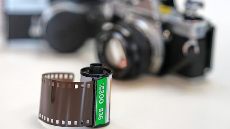 A roll of film sits in front of analogue cameras.