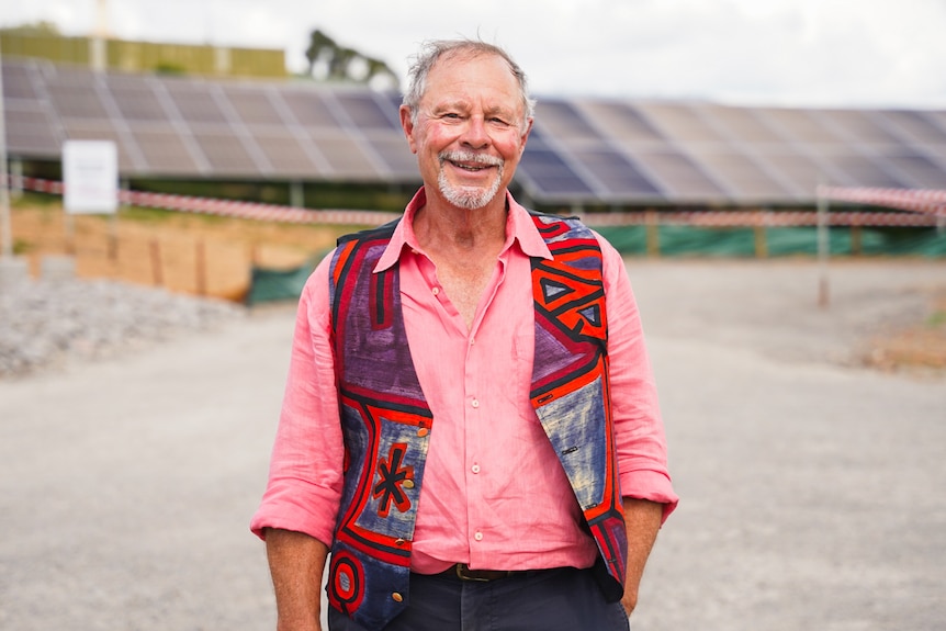 Man in pink shirt smiling in front of solar panels