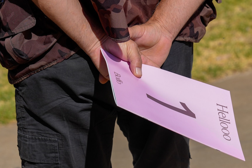 A person holds a pink card with a number 1 and Hellooo written on it