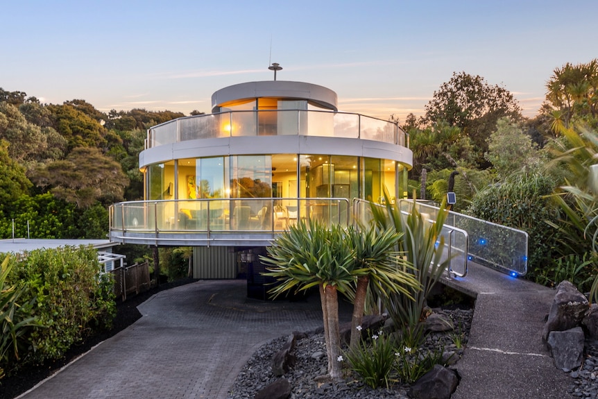 A round house with two levels on a pedestal is lit up inside with mostly glass walls.