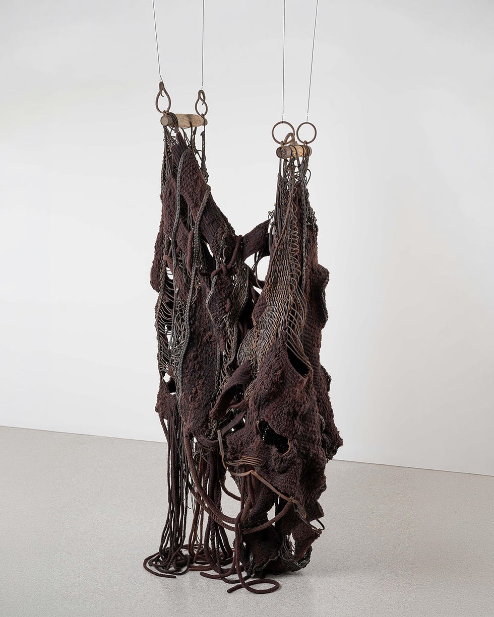 Hanging textile artwork with textured elements and metal components.