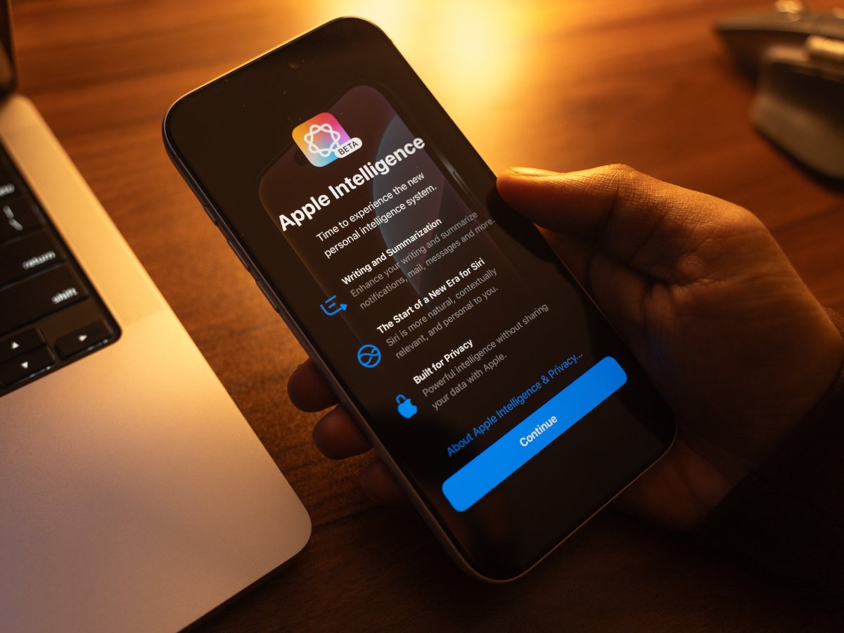 A hand holding an iPhone with an 'Apple Intelligence' pop-up with details on the technology.