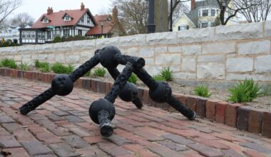 A black ball and socket robot walks on four limbs down a brick path with houses in the background