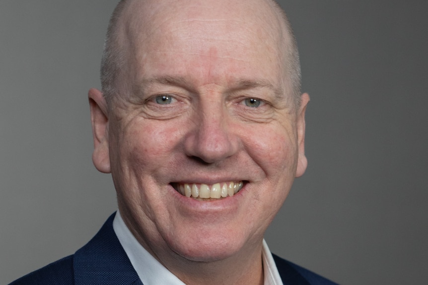 Kevin in a suit, smiling, in front of a blank background, bald, Caucasian man.