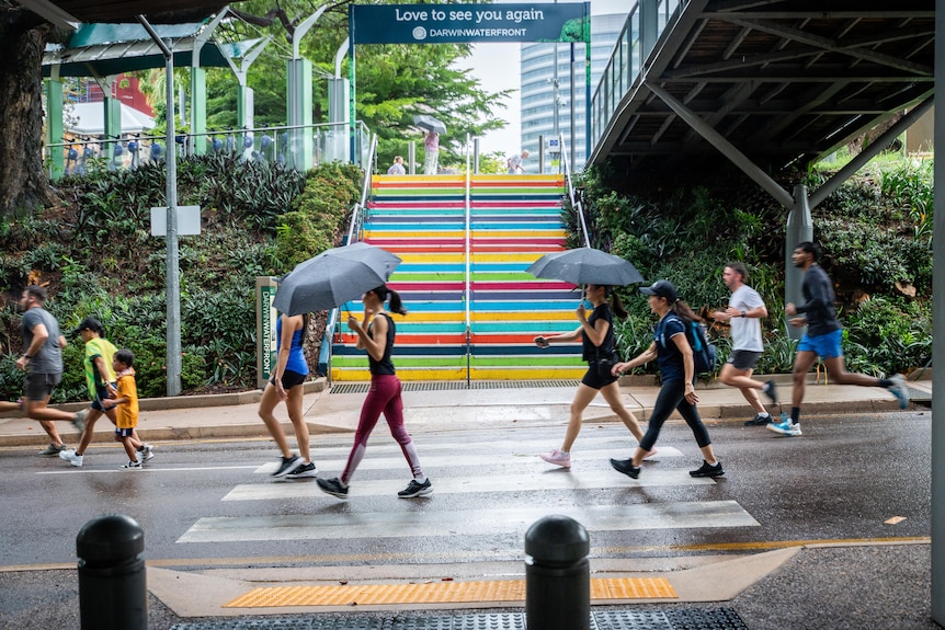 Peopl walking and running with umbrellas past brightly coloured stairs