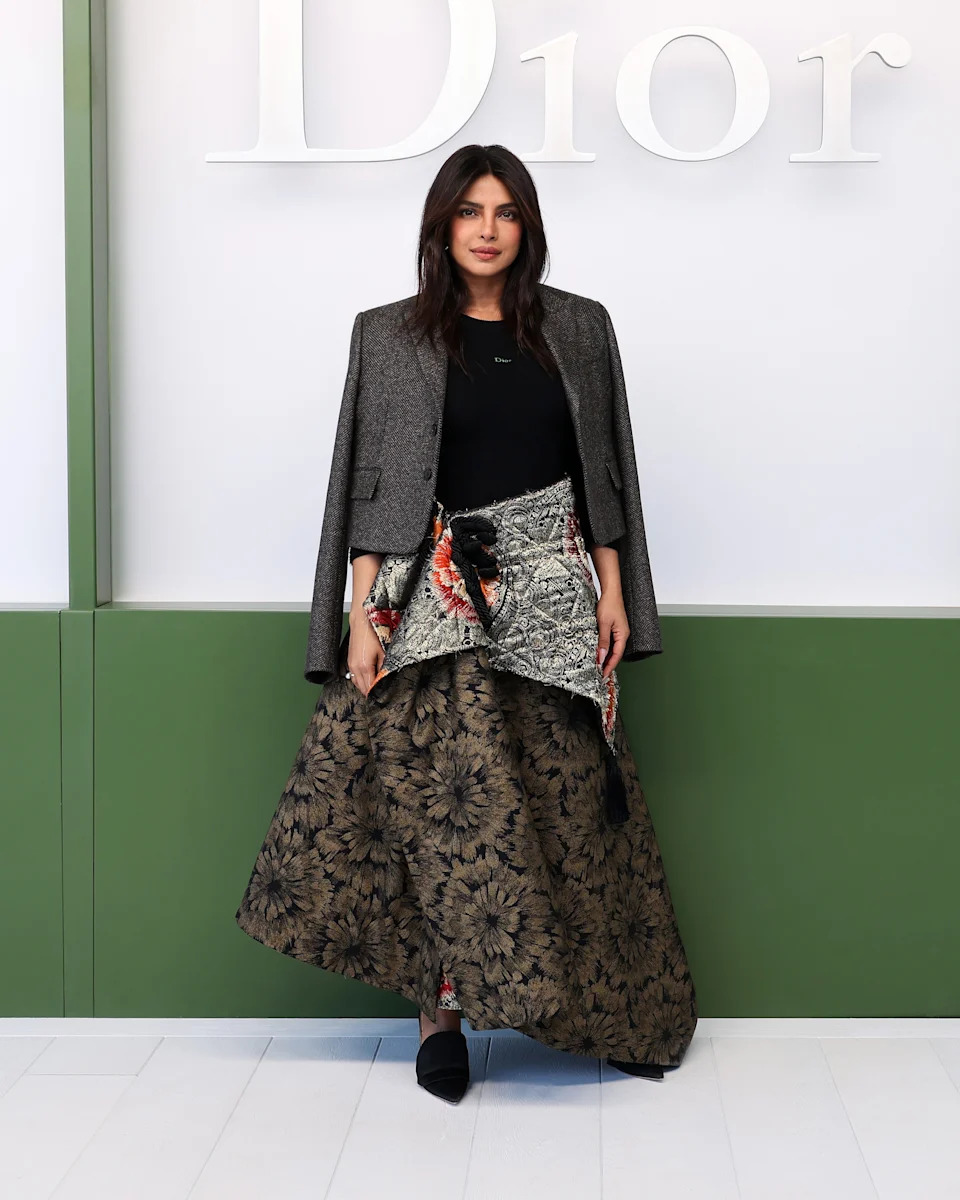 Person in elegant ensemble with a stylish patchwork skirt and blazer stands in front of "Dior" signage