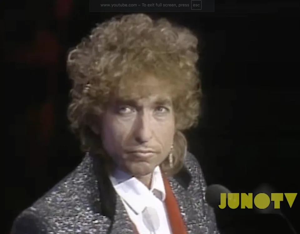 A person with curly hair in a glittery jacket appears to be at an event, facing the camera