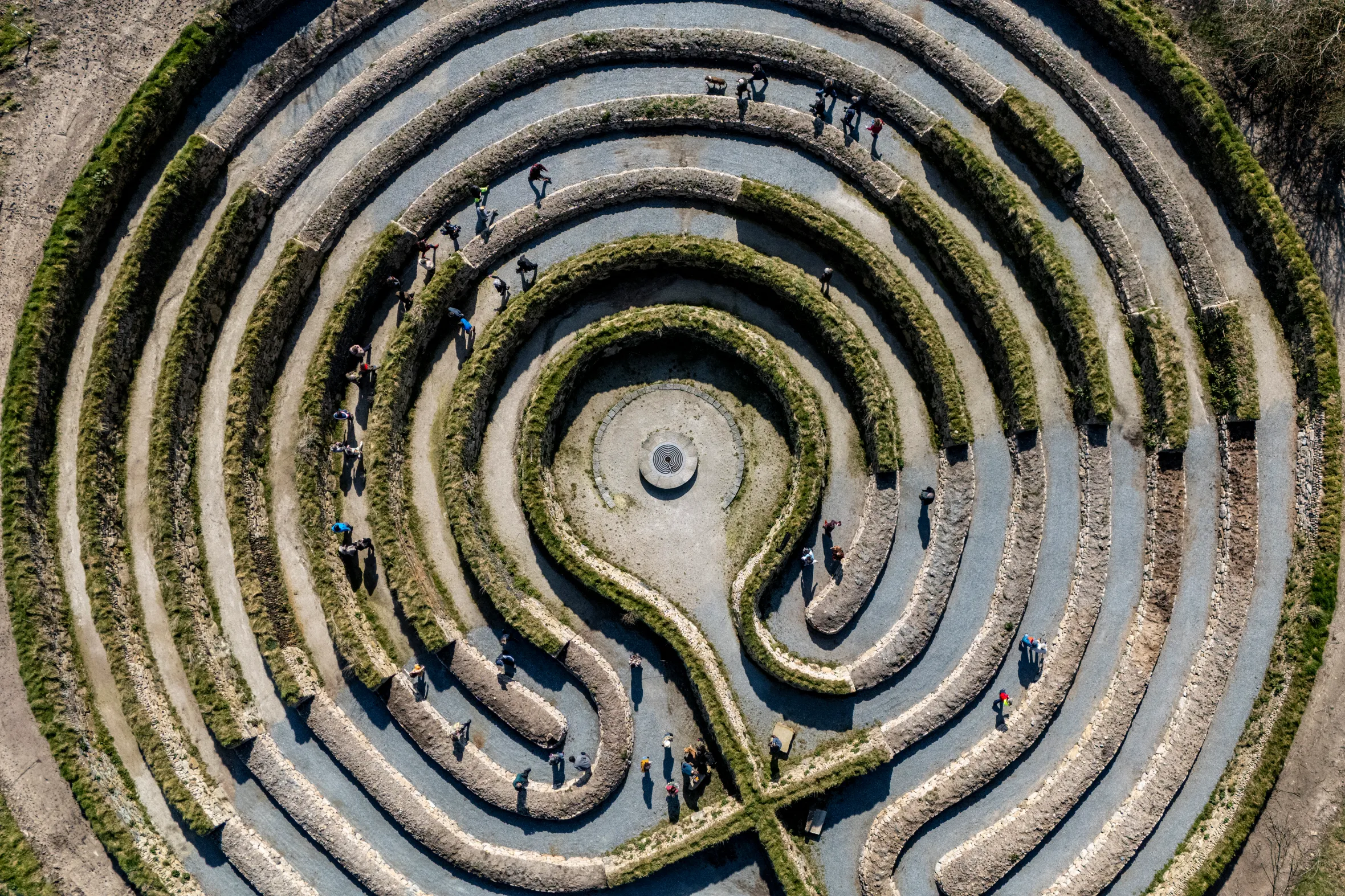 Aerial view of people walking through the Kerdroya labyrinth, an outdoor art installation of concentric, grass-edged stone paths.