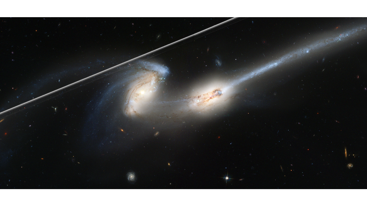 A view of two interacting galaxies in space. There's a white streak to the top left of the image.