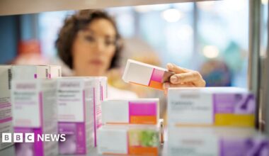 A woman, not in focus, handles different packets of tablets in a pharmacy setting