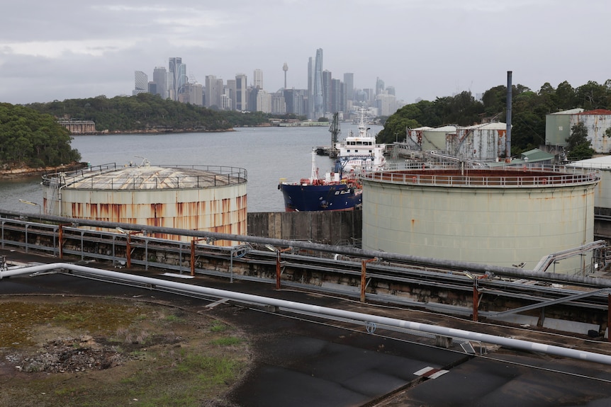 An oil tanker docked behind large storage silos.